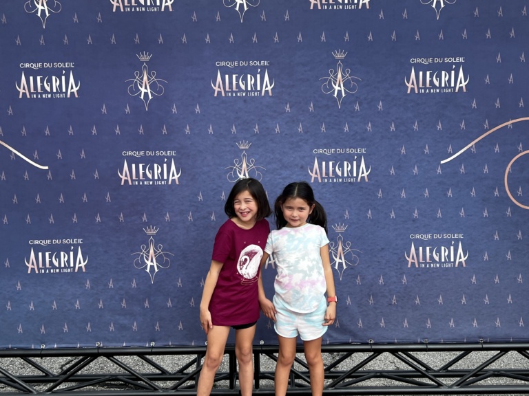 Two girls posing in front of a step-and-repeat backdrop at an event