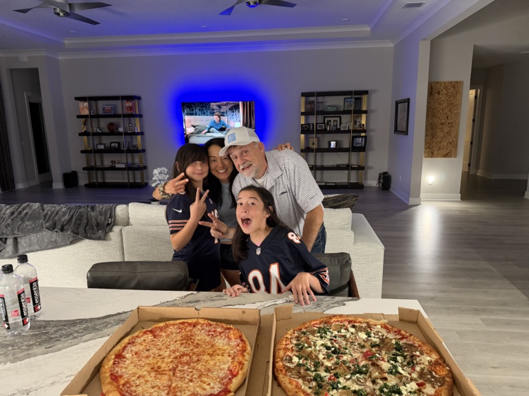 The family on a couch with two large pizzas