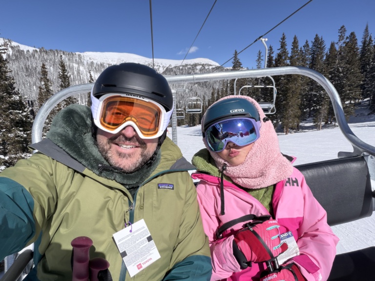 A father and daughter riding a ski lift in goggles