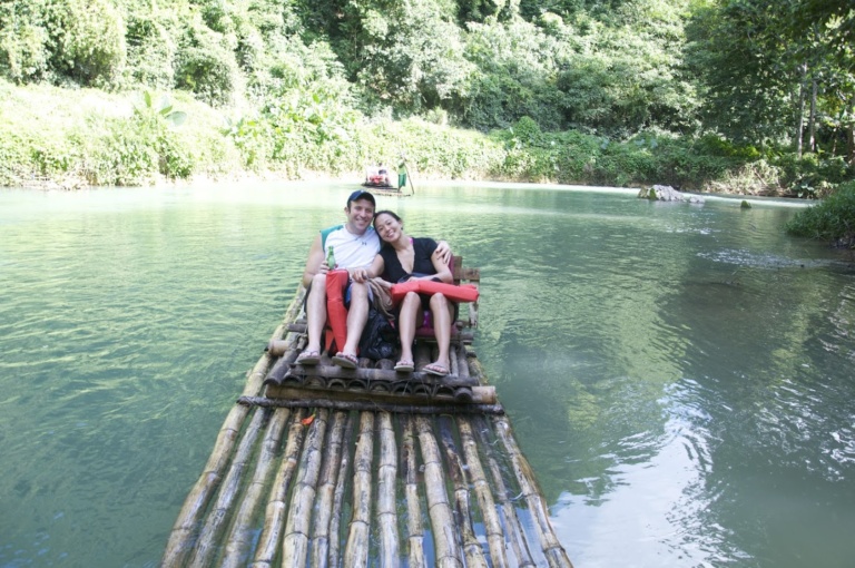 Two people riding a bamboo raft down a green river