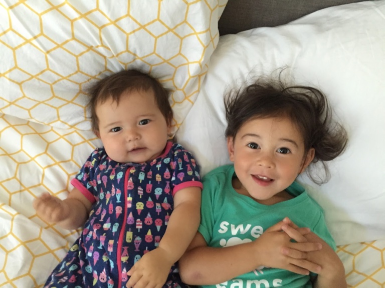 Two babies lying side by side on a bed
