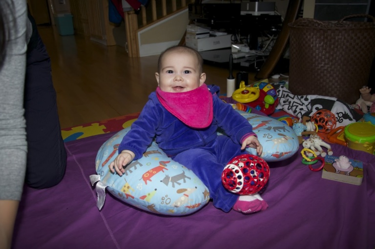 A baby sitting with toys on a floor cushion