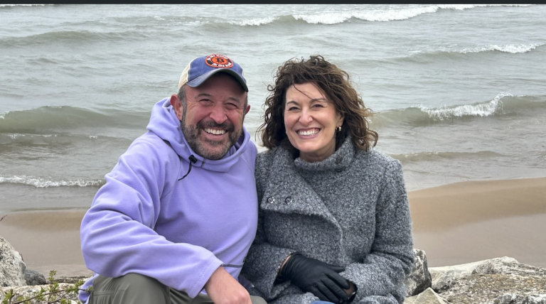 A couple bundled in jackets sitting on a windy beach