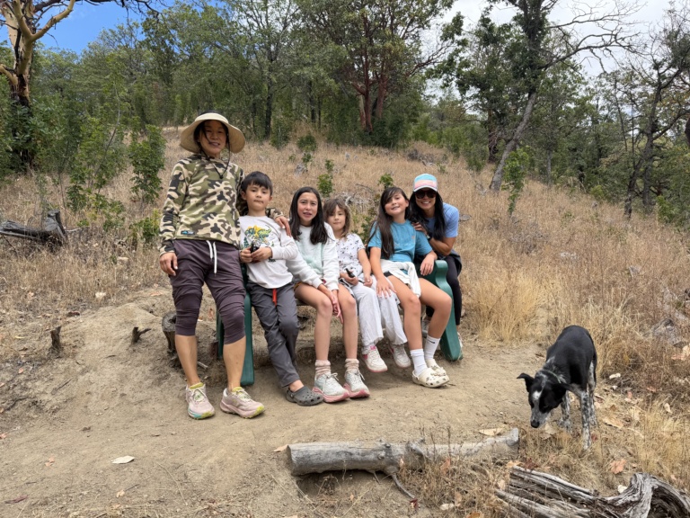 A large family group posing on a dry hillside trail with a dog