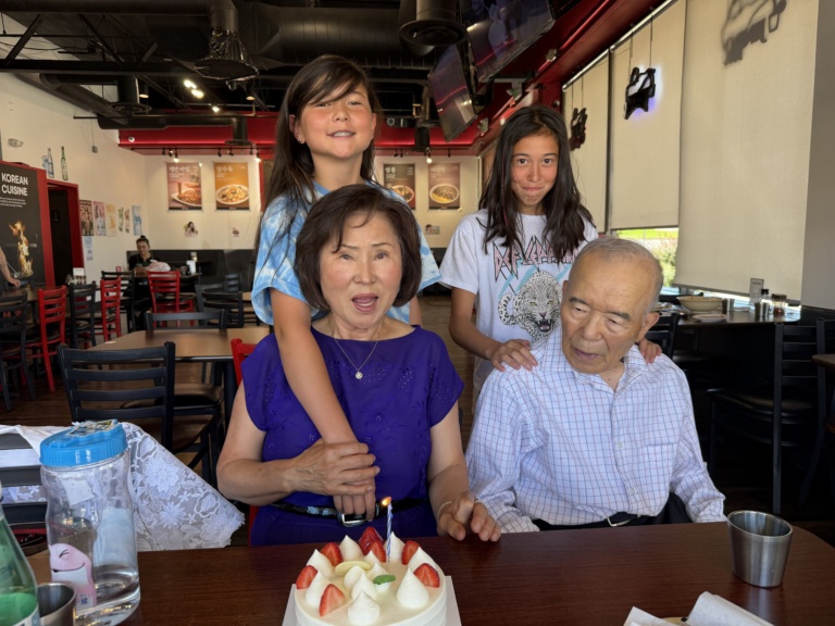 The family gathered around a lit birthday cake at a restaurant
