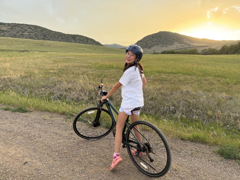 A girl on a bicycle on a grassy hilltop at sunset