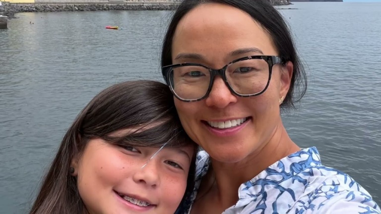 A mother and daughter smiling with water behind them